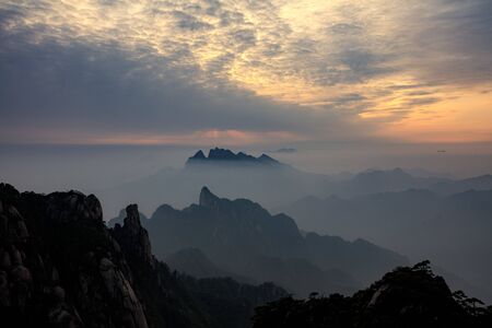 Tree silhouettes during sunset, Vibrant red and orange sky, mountains and horizon. Sanqing Mountain in Jiangxi Province, China. Mist and Fog in the distance, pine tree silhouettes.の写真素材