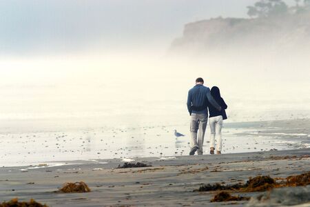 Young couple in love walking on a beach at sunset on a foggy dayの写真素材