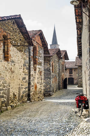 Ricetto of Candelo (Biella, Piedmont, Italy) - Typical street in the medieval village and a bicycle with red black bagsの写真素材