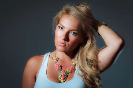 A blonde latina girl in a blue tank top and a big colorful necklace.の写真素材
