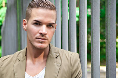 Portrait of  a beautiful young man outdoors against iron gate