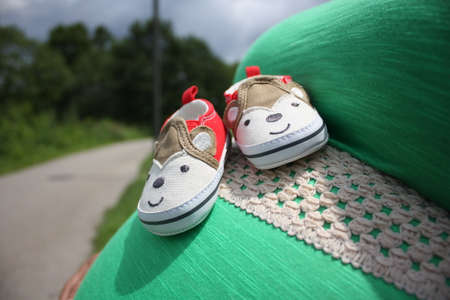 baby's first pair of shoes resting on mother's baby bumpの写真素材