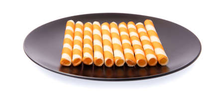 dish of Striped wafer rolls filled with orange isolated on white background