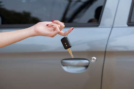 Hand holding car keys with car on backgroundの写真素材