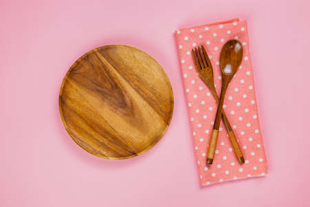 wood plate with spoon, fork and pink polka dot cloth napkin on pink backgroundの写真素材