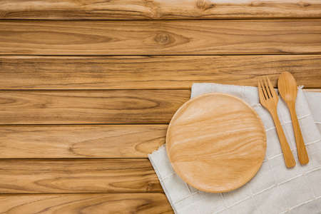 A wood plate rests on a white cloth. There are spoon and fork on wood background