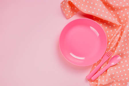 Pink color plastic plate with plastic spoon, fork and pink polka dot Cloth on pink backgroundの写真素材