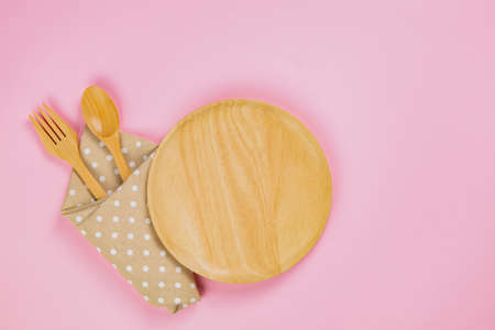 wood plate with spoon, fork and polka dot cloth napkin on pink background