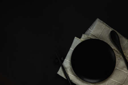 Set black plate with spoon and chopsticks on black background