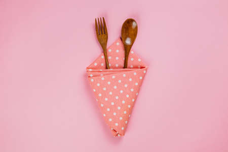 wood spoon, fork and pink polka dot cloth napkin on pink backgroundの写真素材
