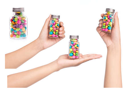 Collection of hand holding bottle of colorful chocolate coated candy isolated on white background.