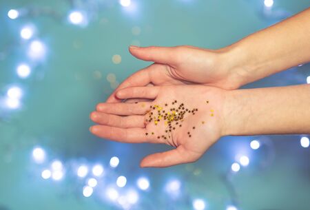 Shiny tiny golden stars in open human palms on a blue background with bokeh. Festive decor,...