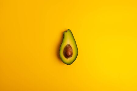 Ripe juicy halved  avocado on a yellow solid background with copy space. Vegan, vegetarian, raw...