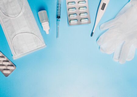 Composition with medical mask, thermometer, syringe, pills and gloves on a blue background....