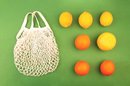 Reusable fruit net bag with oranges and lemons on green background. Zero waste concept. Flat lay.の写真素材