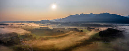 Aerial Panorama view of autumn sunset in mountains with fog and cloud valley landscape. Sun, Haze. Blomberg, Isartal, Bavaria. Duskの写真素材