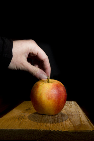 hand grabbing a red and yellow apple on a rustic wooden plank on a black backgroundの写真素材