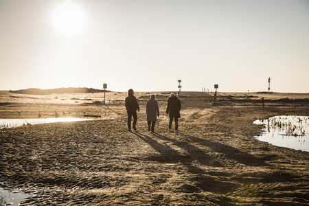 Backlit silhouettes of people walking at sunset by the lagoon in natural reserve Casse de la Belle Henriette, l'Aiguillon sur Mer , Vendee, Franceの写真素材