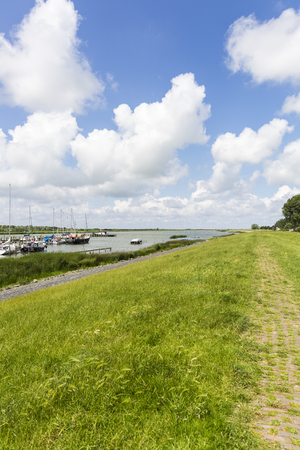 Grass dike in Friesland with blue sky with white cloudsの写真素材