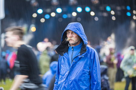 Traena, Norway - July 6 2017: Norwegian man with a moustache and a blue rain coat, hood on, under the rain at Traenafestival, music festival taking place on the small island of Traenaのeditorial素材