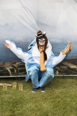 Traena, Norway - July 7 2017: yooung man dressed up with a shark costume eating a snack at Traenafestival, music festival taking place on the small island of Traenaのeditorial素材
