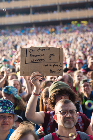 Nyon, Switzerland - 27 July 2019 : crowd of audience cheering in the middle of sop bubbles at concert of Swiss pop singer Stephan Eicher & Traktorkestar. A young man is holding a sign sayin "on chante une chanson ensemble - sous la pluie. Merci" - Let's sのeditorial素材