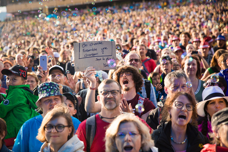 Nyon, Switzerland - 27 July 2019 : crowd of audience cheering in the middle of sop bubbles at concert of Swiss pop singer Stephan Eicher & Traktorkestar. A young man is holding a sign sayin "on chante une chanson ensemble - sous la pluie. Merci" - Let's sのeditorial素材