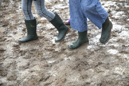 zoom on people walking with rain rubber boots in the mud