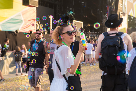 Nyon, Switzerland - 24 July 2019 : a woman with a fancy dress hat is walikng around making soap bubbles shinning in the sunset lightのeditorial素材