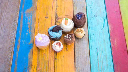 Colorful and tasty cupcakes on a colorful wood tableの写真素材