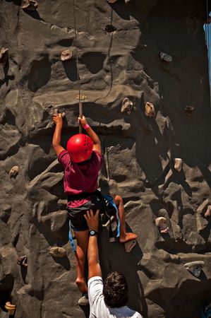 A boy climbing up a rock wall with his father supporting himの写真素材