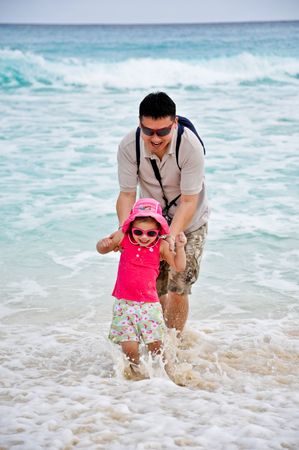 A father and his daughter playing waves at a tropical beachの写真素材