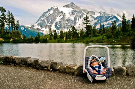 A baby sleeping in a car seat in front of a lake and a mountainの写真素材