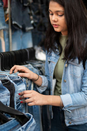 Happy late teen girl looking and buying jeans from outdoor street market of Delhi, India at day time.の写真素材