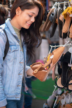 Happy late teen girl looking at sandals display in stand and buying from outdoor street marketの写真素材