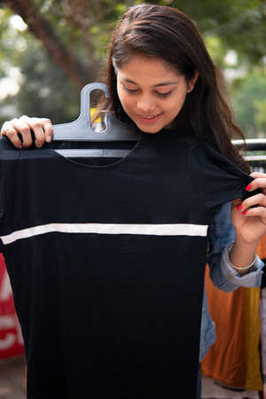 Happy late teen girl looking and buying clothes from outdoor street market