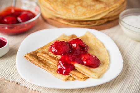 Thin Russian pancakes folded triangle with strawberry sauce on a white plate, close-up, side viewの写真素材