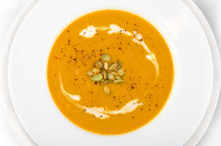 Pumpkin soup with cream, herb and pumpkin seeds in a white plate, top viewの写真素材