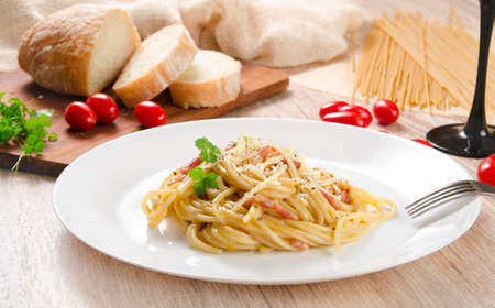 Pasta Carbonara with bacon on a white plate, wooden table, side viewの写真素材