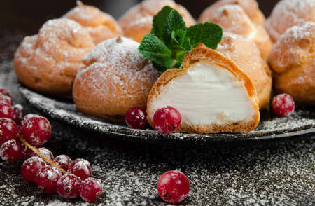 Profiteroles with cream on black plate, dark background, close-upの写真素材