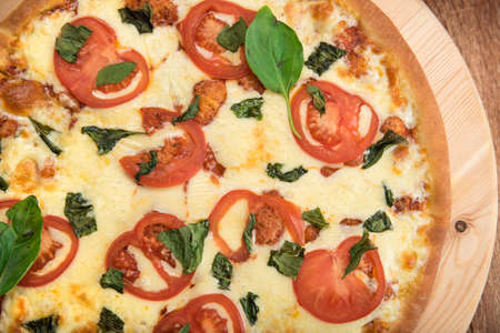 Pizza Margherita with tomatoes, mozzarella and basil on a wooden board, top view, close-upの写真素材