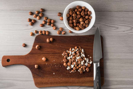 Cut hazelnuts on a wooden board with a knife, ingredients for cooking, wood background, top viewの写真素材