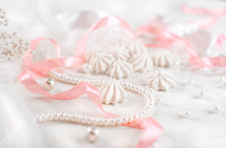 French meringue cookies for wedding background with pearls, pink and white satin ribbons and lace, close-upの写真素材