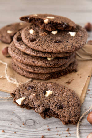 Chocolate cookies with hazelnuts, white chocolate and dark chocolate on parchment, wooden background, vertical, close-upの写真素材