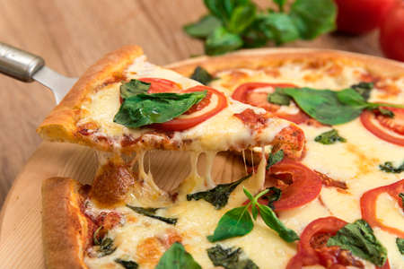 Pizza Margherita with tomatoes, mozzarella and basil on a wooden background, a slice of pizza with cheese stretching, close-upの写真素材