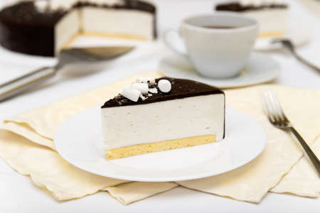 Piece of cake with souffle "Bird's milk", biscuit, mousse and dark chocolate on a white plate, decorated tableの写真素材