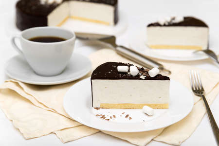 Piece of cake with souffle "Bird's milk", biscuit, mousse and dark chocolate on a white plate, decorated tableの写真素材