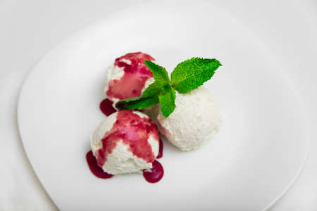 Three scoops of ice cream with strawberry syrup and mint on a white plate, white background, close-up, top viewの写真素材