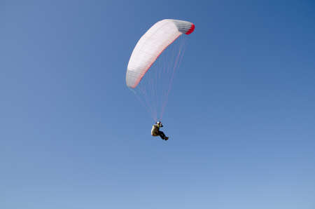 Man jumping with parachute on sky blue backgroundの写真素材