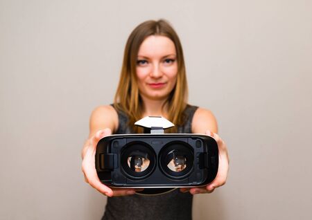 Beautiful girl holding headset of virtual reality in her hand and offering to wear it